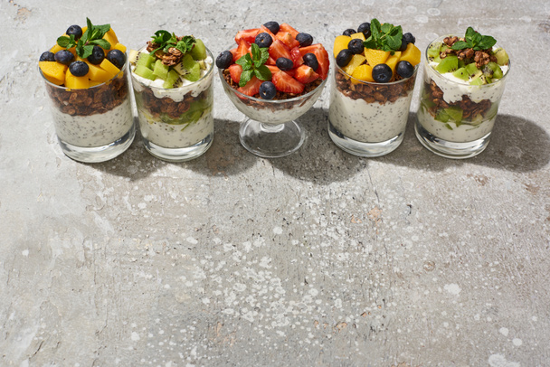 delicious granola in glasses with fruits and berries on grey concrete surface - Fotoğraf, Görsel