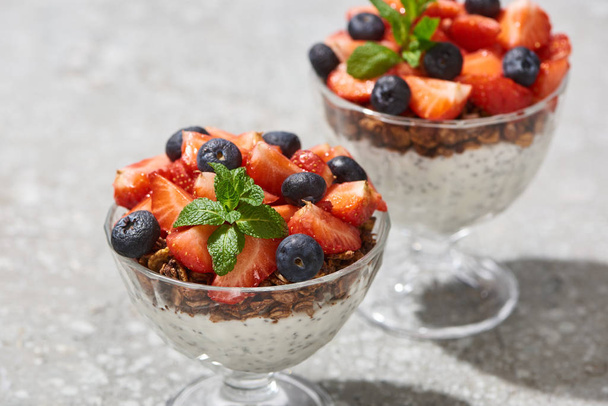 селективний фокус смачної граноли з ягодами та йогуртом з насінням чіа на сірій бетонній поверхні
 - Фото, зображення