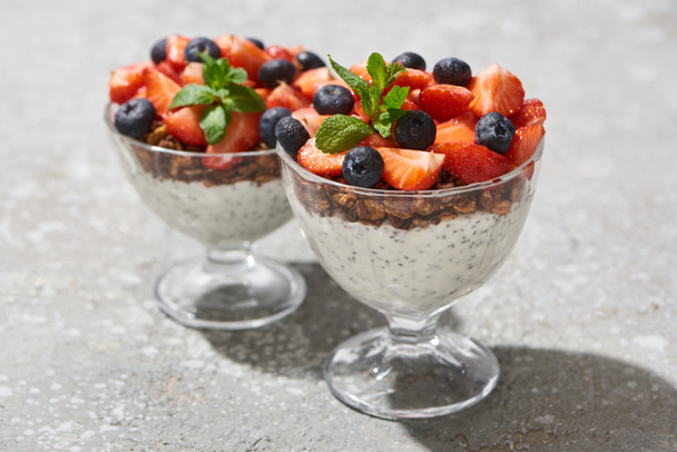 selective focus of delicious granola with berries and yogurt with chia seeds on grey concrete surface - Фото, зображення