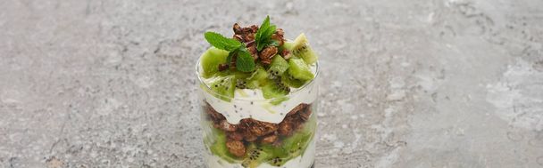 verse granola met kiwi en yoghurt in glas op grijs betonnen oppervlak, panoramisch schot - Foto, afbeelding