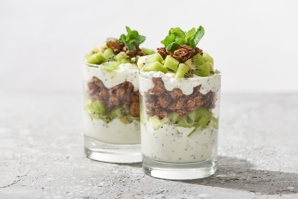 selective focus of fresh granola with kiwi and yogurt on concrete surface isolated on grey - Foto, afbeelding