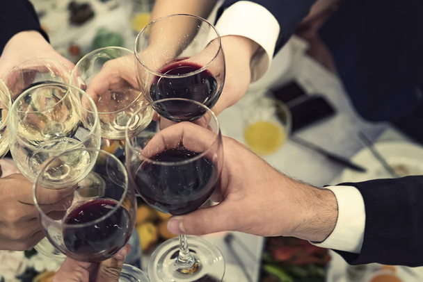 Top-down view of male and female hands with filled glasses of wine above the restaurant tabletop. Drinking toasts and clinking tumblers at a dinner party. Drinking wine at a banquet. Feast an event. - Photo, Image