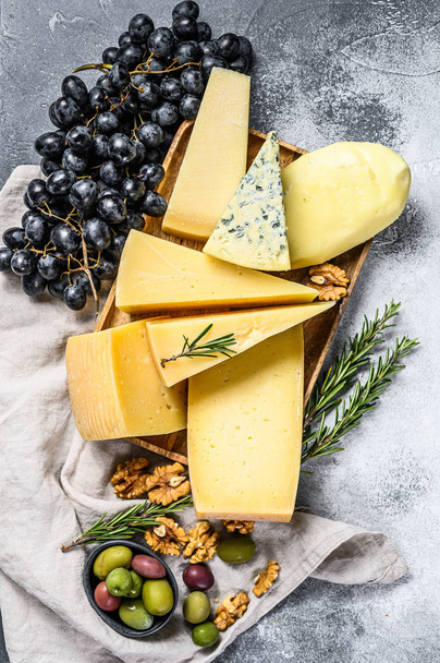 Diferentes pedaços de queijo com azeitonas e uvas. Deliciosos lanches variados. Fundo cinzento. Vista superior - Foto, Imagem