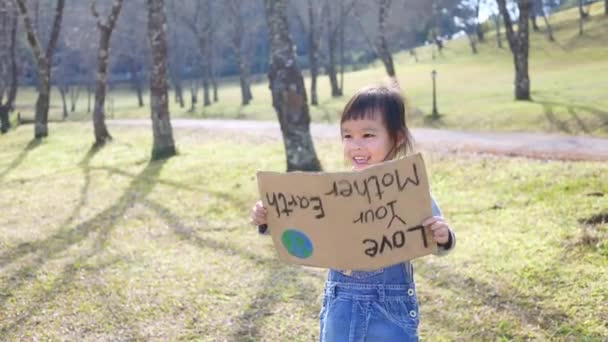 Little Asian girl holding "Love your Mother Earth" Poster on a demonstration due to climate change by plastic pollution. Children standing in the park with a sign to save the world. - Metraje, vídeo