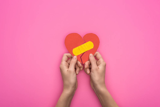 cropped view of holding broken paper heart with patch isolated on pink background - Fotografie, Obrázek