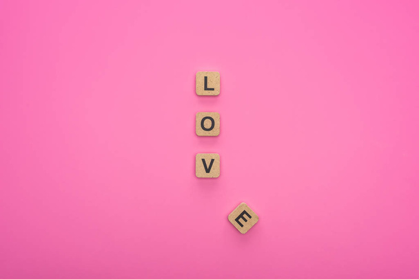 top view of love lettering on wooden cubes isolated on pink background - 写真・画像