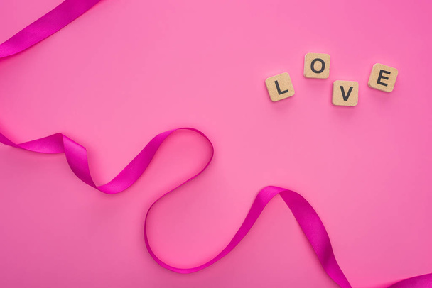 top view of silk curved ribbon and wooden blocks with love lettering isolated on pink - Fotografie, Obrázek