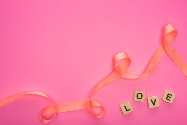 top view of curved ribbon and wooden blocks with love lettering isolated on pink - Photo, Image