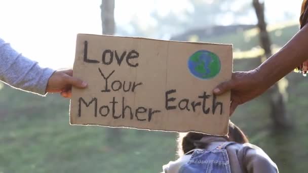Ręce trzymające plakat "Love your Mother Earth" na demonstracji z powodu zmian klimatycznych spowodowanych zanieczyszczeniem plastiku. Ludzie stojący w parku ze znakiem ratowania świata. - Materiał filmowy, wideo
