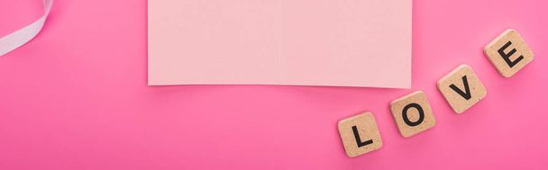 top view of empty paper card with ribbon and wooden blocks with love lettering isolated on pink, panoramic shot - Foto, afbeelding