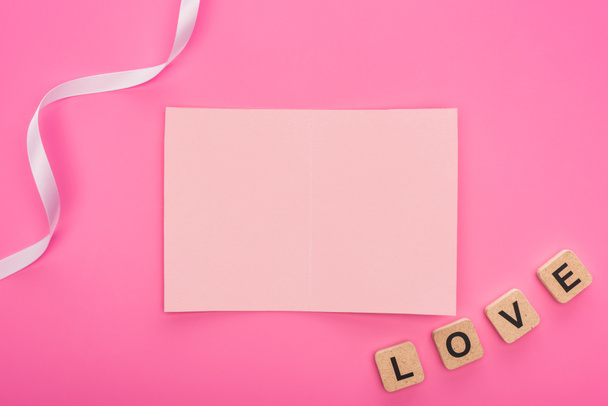vista superior de la tarjeta de papel vacía con cinta y letras de amor en cubos de madera aislados en rosa
 - Foto, Imagen