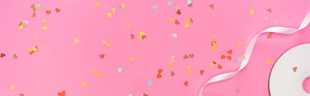 top view of valentines confetti, empty compact disk, ribbon on pink background, panoramic shot - Photo, Image
