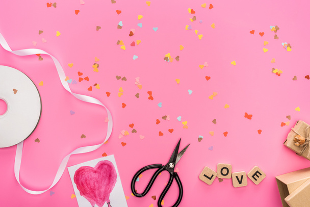 top view of valentines confetti, empty compact disk, scissors, gift boxes, greeting card and love lettering on wooden cubes on pink background - 写真・画像