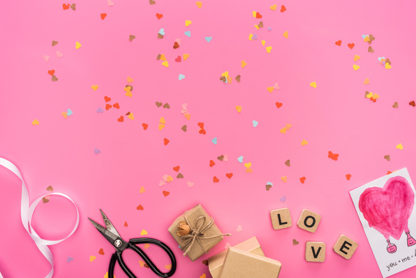 top view of valentines confetti, empty compact disk, scissors, gift boxes, greeting card and cubes with love lettering on pink background - Photo, Image