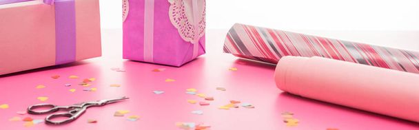 valentines confetti, scissors, wrapping paper, gift boxes on pink surface isolated on white, panoramic shot - Photo, image