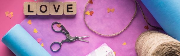 top view of valentines decoration, scissors, wrapping paper, twine, love lettering on wooden cubes on pink background, panoramic shot - Photo, image