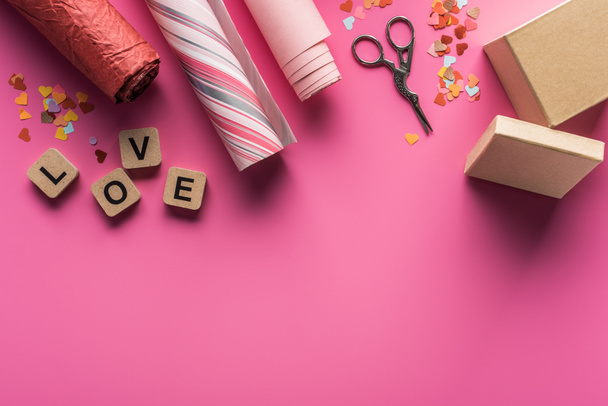 vista superior da decoração dos namorados, tesoura, caixa de presente, papel de embrulho e letras de amor em cubos de madeira no fundo rosa
 - Foto, Imagem