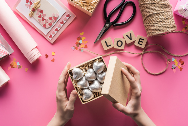 vue partielle de la femme tenant boîte cadeau avec des coeurs d'argent près de fournitures de bricolage valentines sur fond rose
 - Photo, image