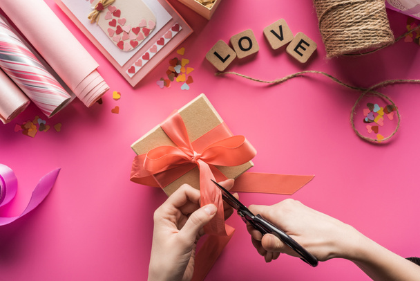 cropped view of woman cutting ribbon while making valentines gift on pink background - Zdjęcie, obraz