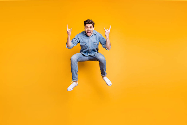Full length body size photo of cheerufl shouting guy with fingers horned wearing sneakers showing rock horned fingers sign jumping isolated vivid color background - Fotografie, Obrázek