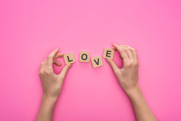 partial view of woman holding cubes with love lettering on pink background - Foto, Imagem
