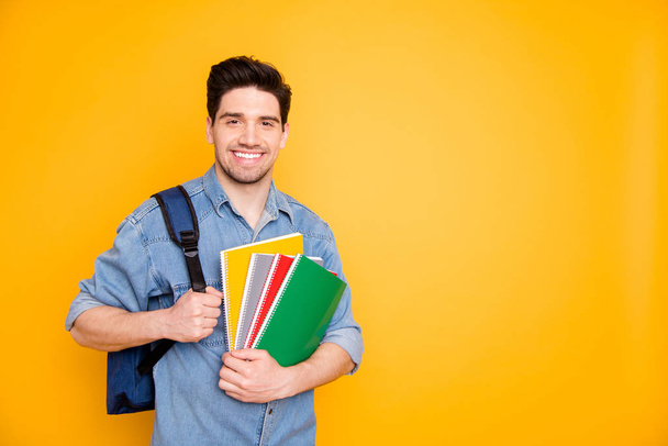 Photo of cheerful positive man near empty space holding colorful notepads with rucksack behind back isolated bright color background - Foto, immagini