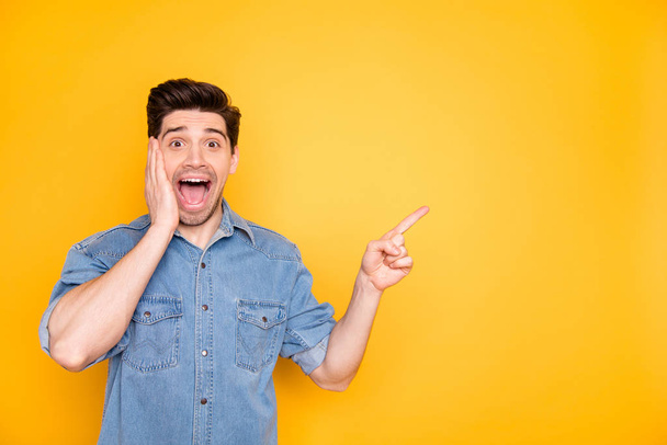 Photo of cheerful excited ecstatic crazy man in jeans denim expressing overjoyed emotions on face screaming about sales pointing into empty space isolated vivid color background - Foto, imagen