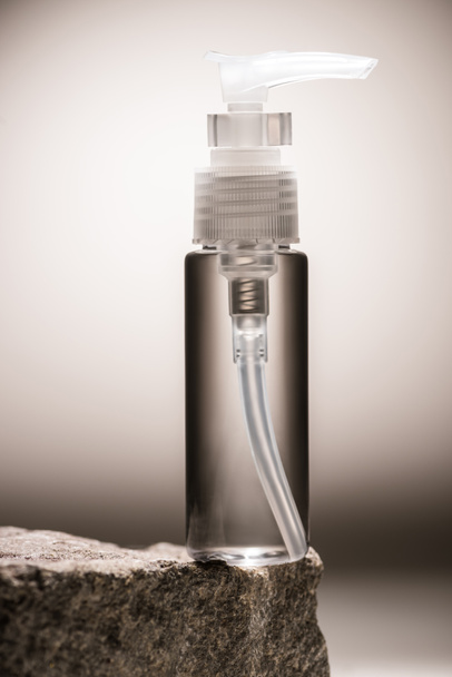 botella cosmética dispensador transparente en piedra sobre fondo oscuro con luz de fondo
 - Foto, imagen