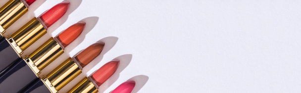 Draufsicht auf verschiedene Lippenstifte in Luxusröhren in einer Reihe auf weißem Hintergrund, Panoramaaufnahme - Foto, Bild