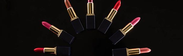 top view of assorted lipsticks in luxury tubes arranged in circle isolated on black, panoramic shot - Photo, Image
