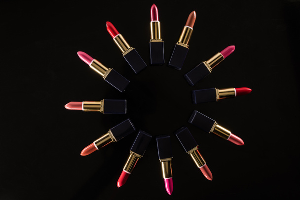 vista superior de batons variados em tubos de luxo dispostos em círculo isolado em preto
 - Foto, Imagem