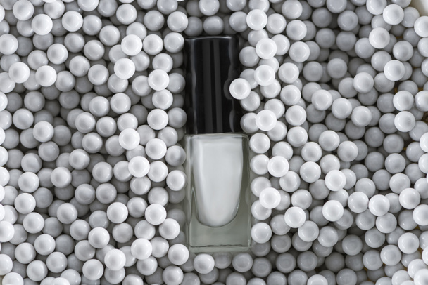top view of white nail polish in bottle among grey decorative beads - Fotó, kép
