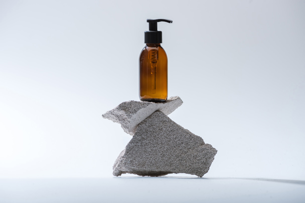 dispensador botella cosmética sobre piedras sobre fondo blanco con luz de fondo
 - Foto, Imagen