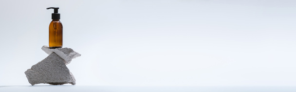 диспенсер косметическая бутылка на камнях на белом фоне с задним светом, панорамный снимок
 - Фото, изображение