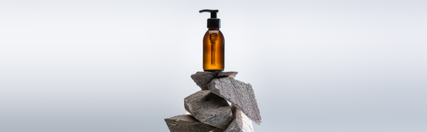 dispensador botella cosmética sobre piedras sobre fondo blanco con luz de fondo, plano panorámico
 - Foto, Imagen
