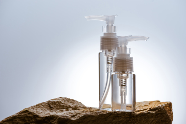 dispensador de botellas de cosméticos en piedra sobre fondo blanco con luz de fondo
 - Foto, imagen