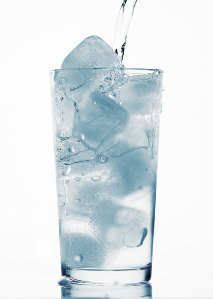 Gießen von Wasser in ein Glas voller Eiswürfel, weißer Hintergrund, blau getönter Gegenstand - Foto, Bild