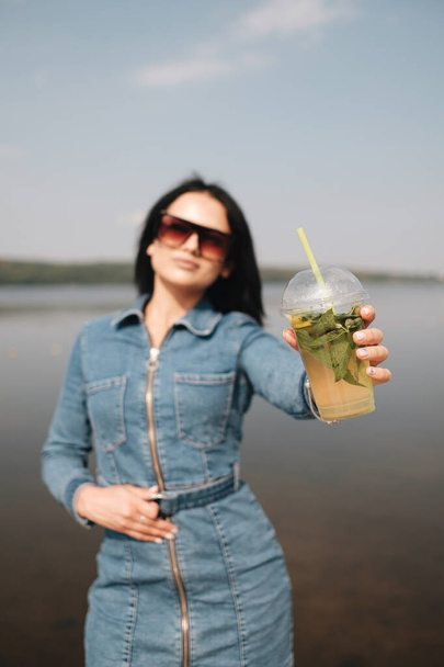 ein schönes brünettes Mädchen in Jeans Overalls trinkt Cocktail - Foto, Bild
