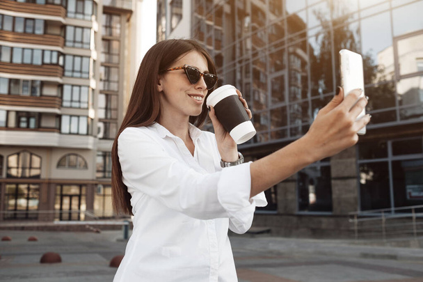 Close Up Portrait of One Fashionable Girl Dressed in Jeans and White Shirt Drinking Coffee and Using Her Smartphone, Business Lady, Woman Power Concept - Foto, Imagen