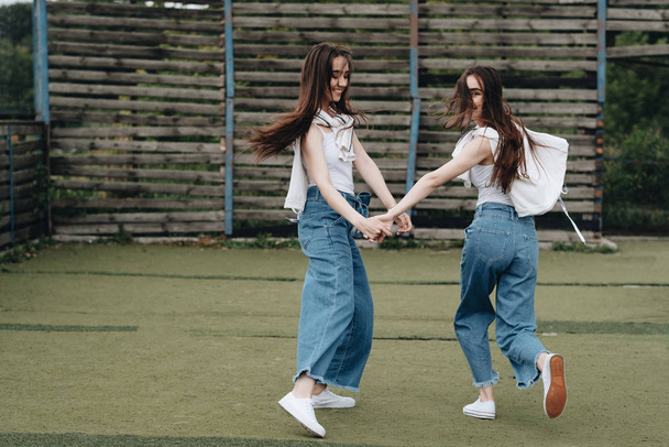 Portrait of Two Young Brunette Twins Sisters Dressed Alike in Jeans and White T-shirt, Best Friends Forever Concept - Valokuva, kuva
