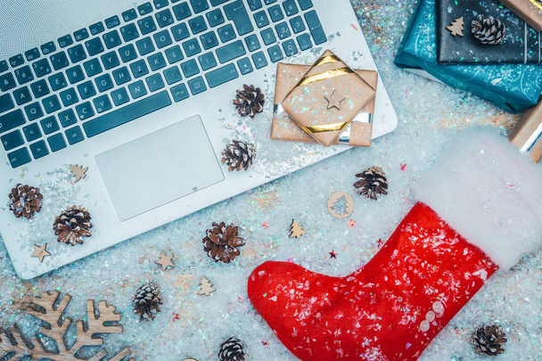 Flat lay or top view of laptop keyboard, gifts and red Santa Claus sock on fake snow. Online shopping for christmas holiday concepts. - Photo, Image