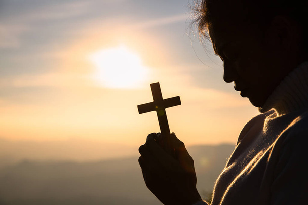 Silhouet van christelijke jonge vrouwen biddend met een kruis bij de zon - Foto, afbeelding