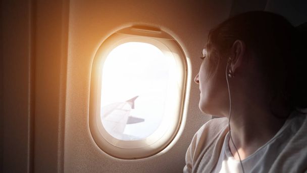 Portrait of young woman is looking at plane window. - Zdjęcie, obraz