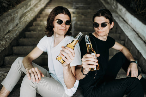 Dvě stylová dvojčata se baví pitím piva na schodech - Fotografie, Obrázek