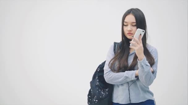 Emotional young asian girl is on the phone, discussing some problems, waving her hands, looking upset. Backpack over her shoulder. - Video