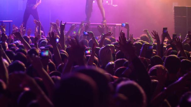 Energetische mensen dansen met hun handen omhoog bij het concert - paarse verlichting - Foto, afbeelding