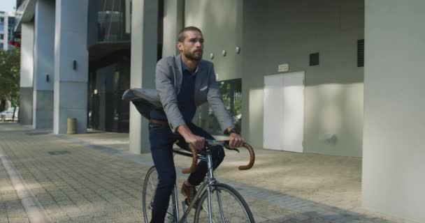 Front view of a young Caucasian businessman on the go in the city, riding a bike in the street, slow motion - Filmagem, Vídeo