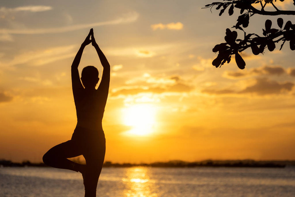 Sziluett egészséges nő jóga egyensúly test gyakorlása létfontosságú meditáció és gyakorlás a szikla szabadban a strandon naplementekor. Egészséges és életmód koncepció.  - Fotó, kép