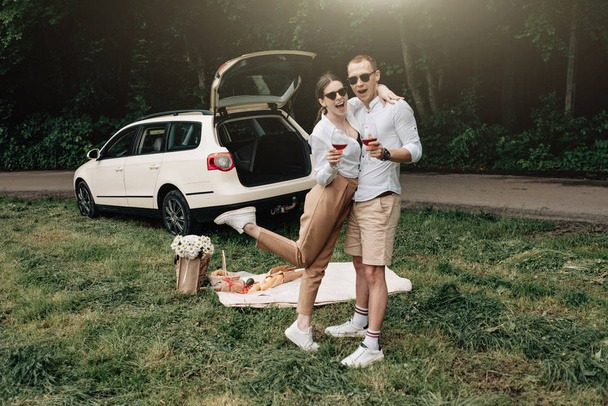 Молодая счастливая пара одета одинаково в белую футболку с весельем возле автомобиля, выходные за городом, праздники и дорожные поездки концепции
 - Фото, изображение