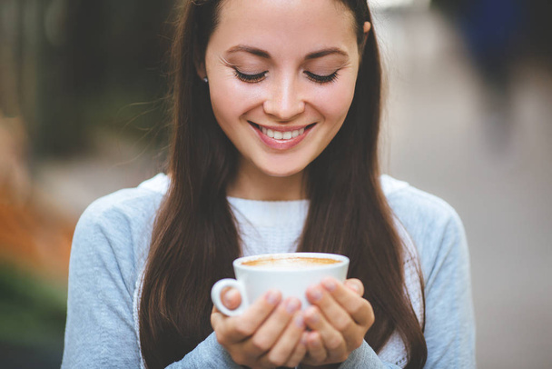 close-up van een vrouw handen houden van een hete koffie kopje buiten met buiten in de achtergrond. - Foto, afbeelding